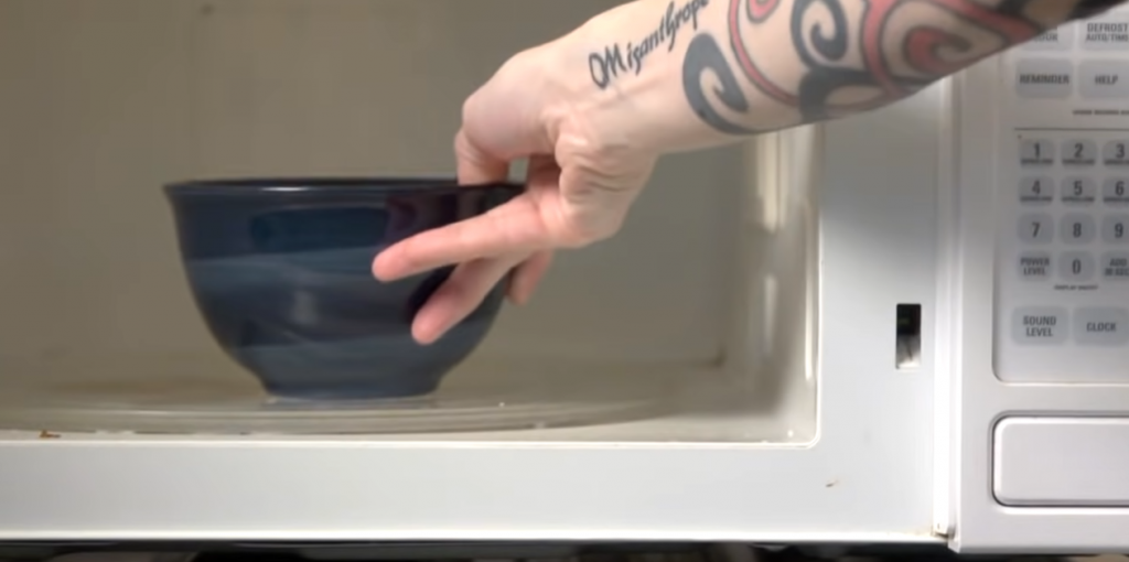 hand with tattoos putting bowl in microwave