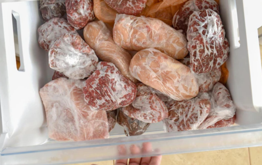 high-angle shot of freezer drawer full of frozen meat wrapped in plastic film