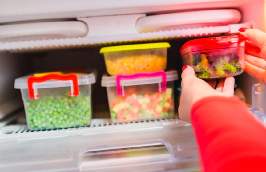 woman placing container with frozen mixed vegetables in freezer.
