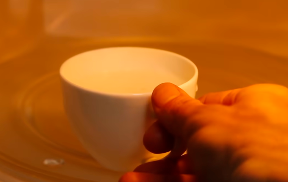 hand putting mug with an egg In microwave